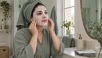 زنی در حال تنظیم ماسک ورقه‌ای صورت در فضایی با رنگ‌های سبز ملایم و کرم؛ تصویر مفهومی