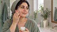 زنی با سرخی خفیف گونه در حال استفاده ملایم از مرطوب‌کننده مقابل آینه؛ تصویر مفهومی پوست حساس
